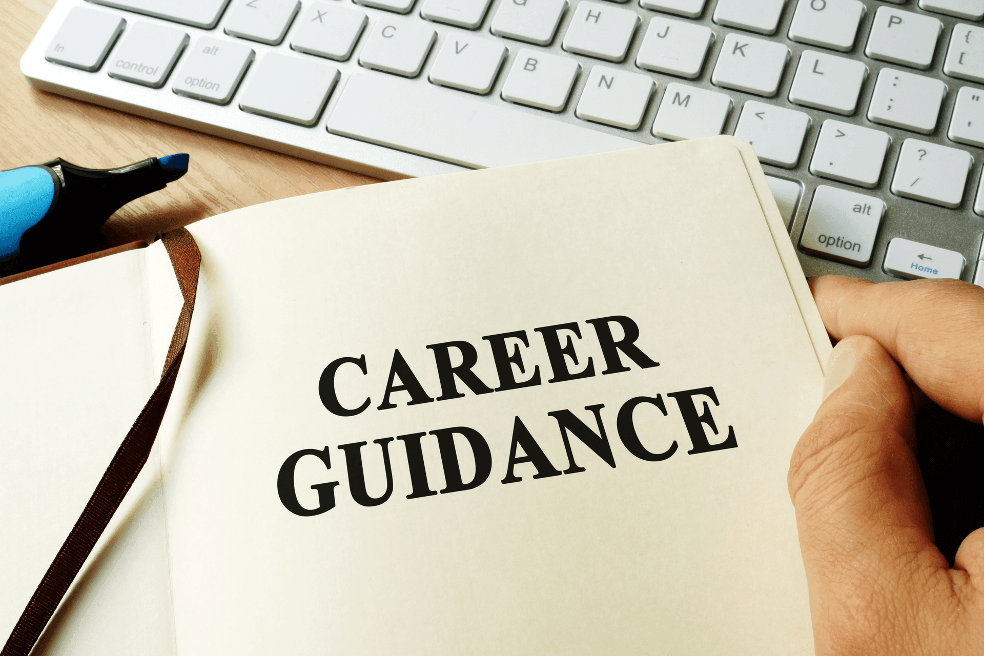 Open book with 'Career Guidance' text beside a keyboard and highlighter on a desk.